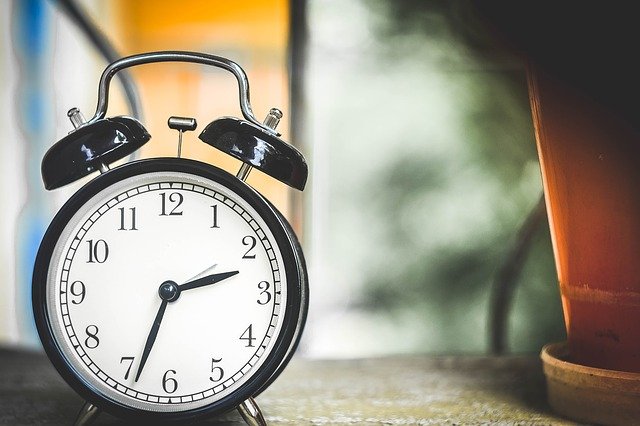 An old fashioned alarm clock sitting on a side table. Photo by obpia on Pixabay, all rights reserved to the owner.